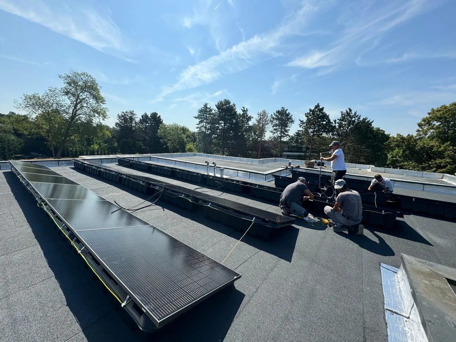 Trois installateurs fixant un champ de panneaux solaires sur une toiture terrasse, par ciel dégagé.